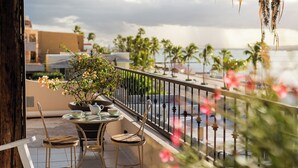 Ein Balkon mit Tisch und Stühlen, einem Blumentopf und Blick auf Palmen sowie ein Gewässer.