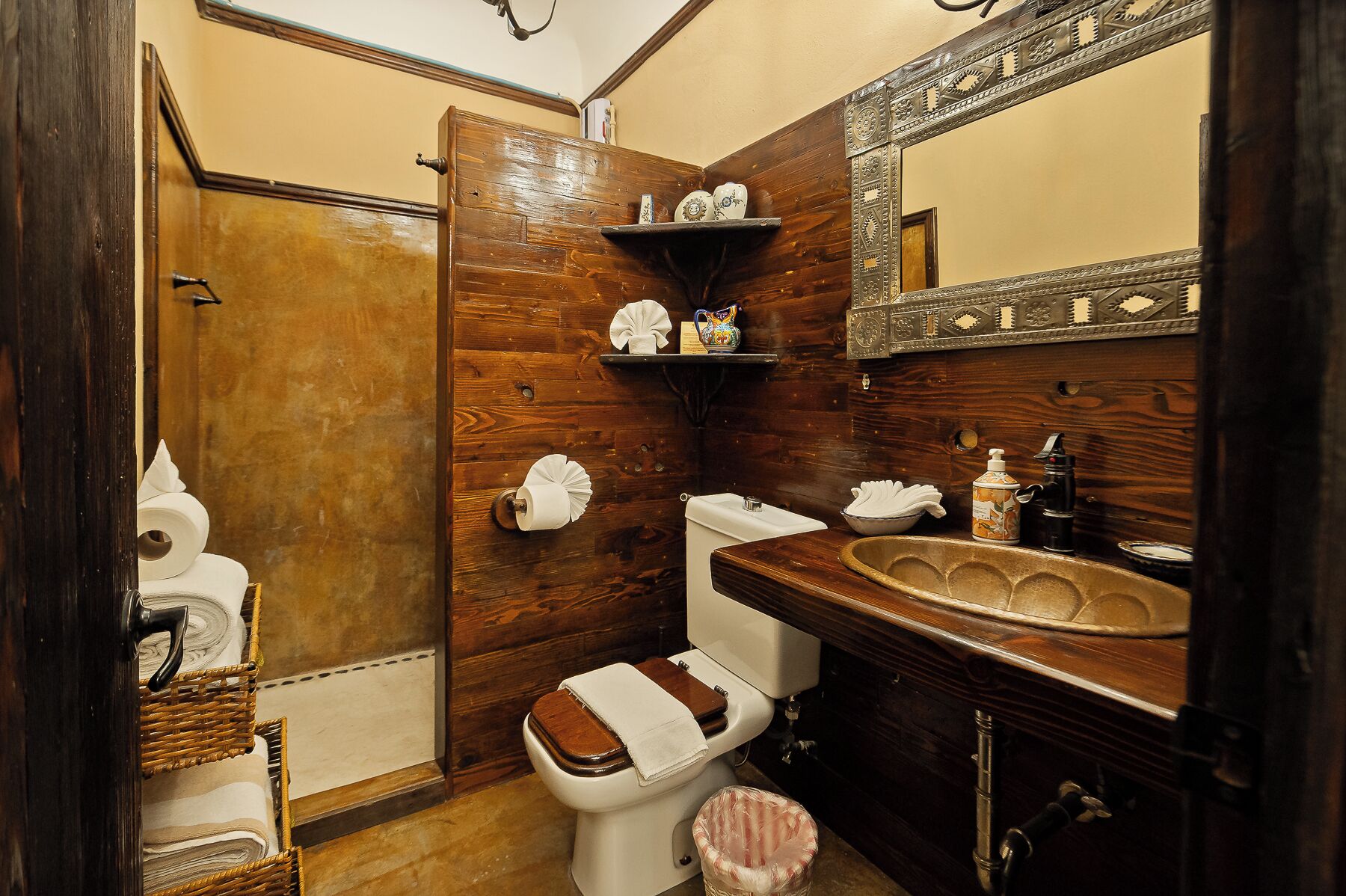 Un baño con tocador de madera, inodoro y estante con artículos de aseo.