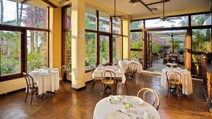 Ein Restaurant mit runden Tischen, großen Fenstern mit Blick ins Grüne und einem Deckenventilator.