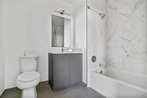 Ein modernes Badezimmer mit Toilette, Waschtisch, Spiegel und Badewanne.