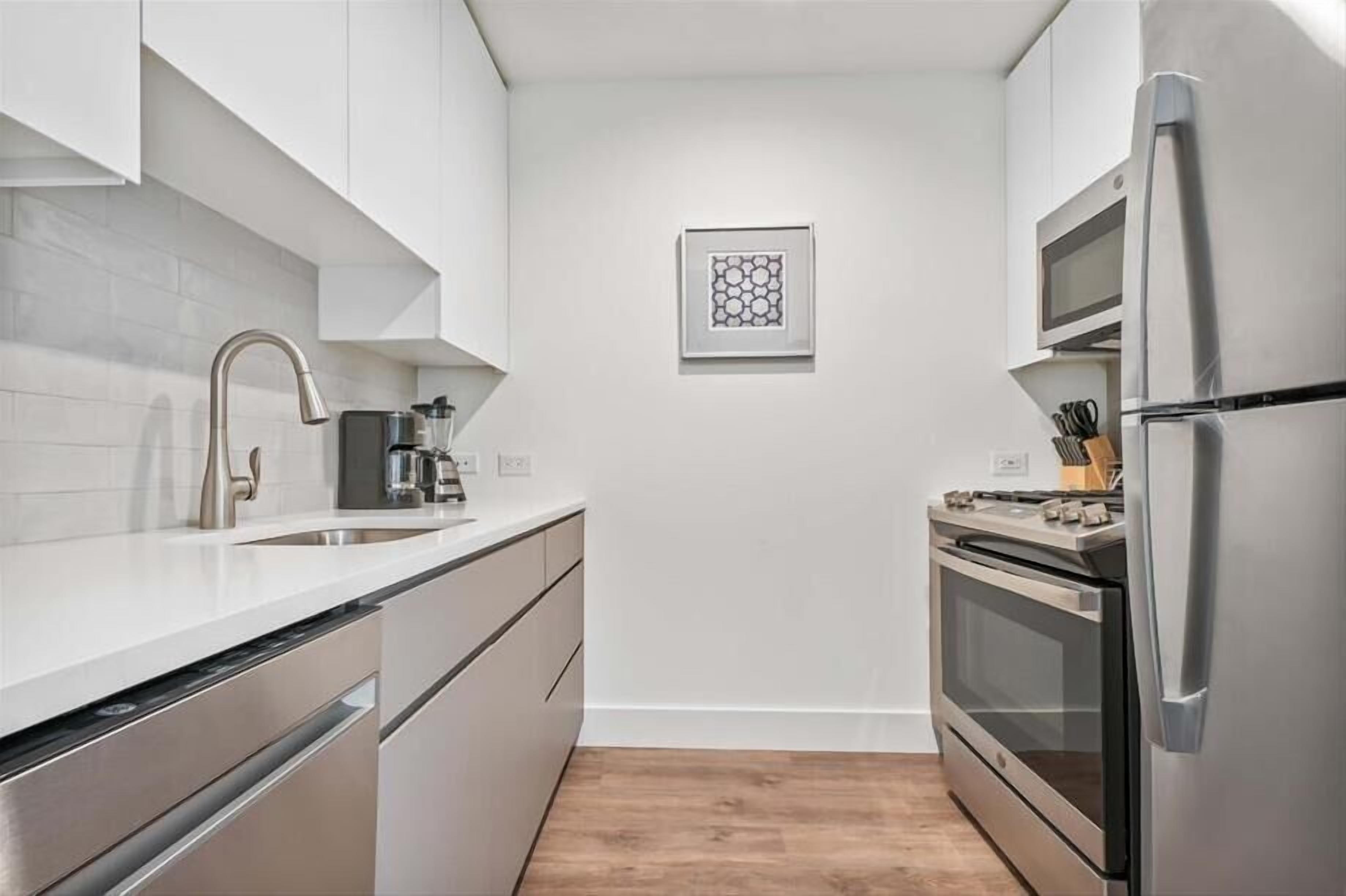 Una cocina moderna con armarios blancos, electrodomésticos de acero inoxidable y suelo de madera.