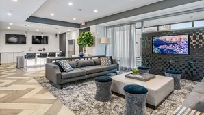 Un salon moderne avec un canapé, un pouf et un téléviseur. Il y a également un coin cuisine avec un bar et des chaises.