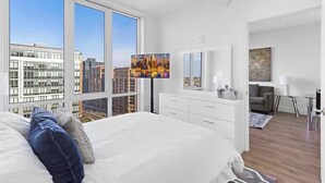 Moderni hotellihuone, jossa on suuret ikkunat, sänky, työpöytä, tuoli ja televisio.