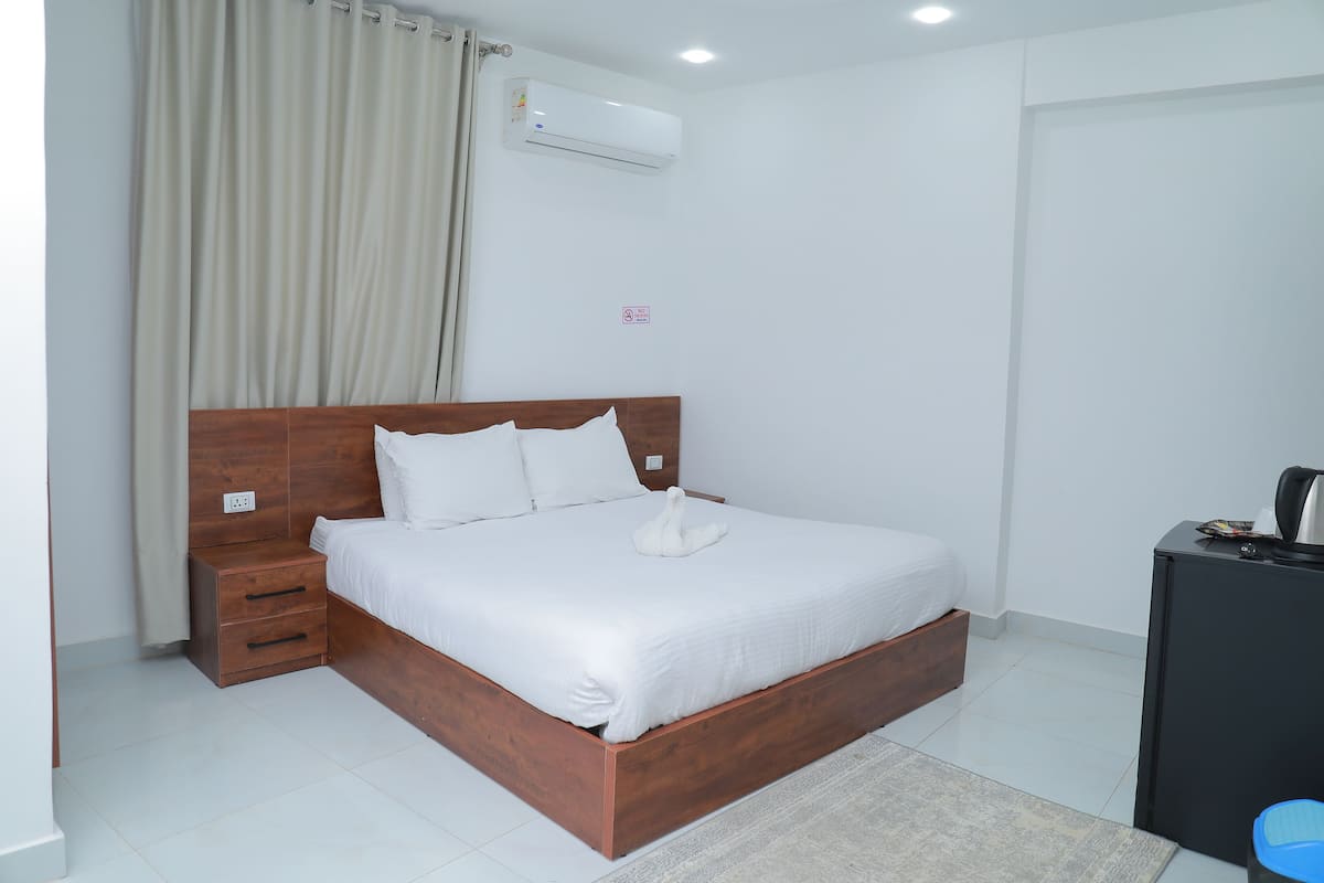A neatly made bed with a wooden headboard, a bedside table, and a small drawer unit.