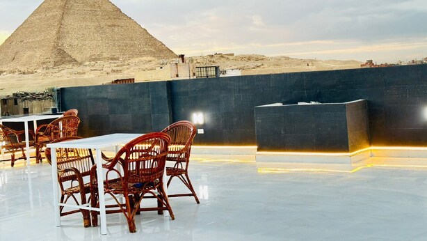Un comedor con sillas de mimbre y una mesa, una pirámide al fondo y vista al desierto.