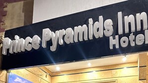 Exterior del Hotel Prince Pyramids Inn, con un letrero destacado y un cartel de las pirámides.