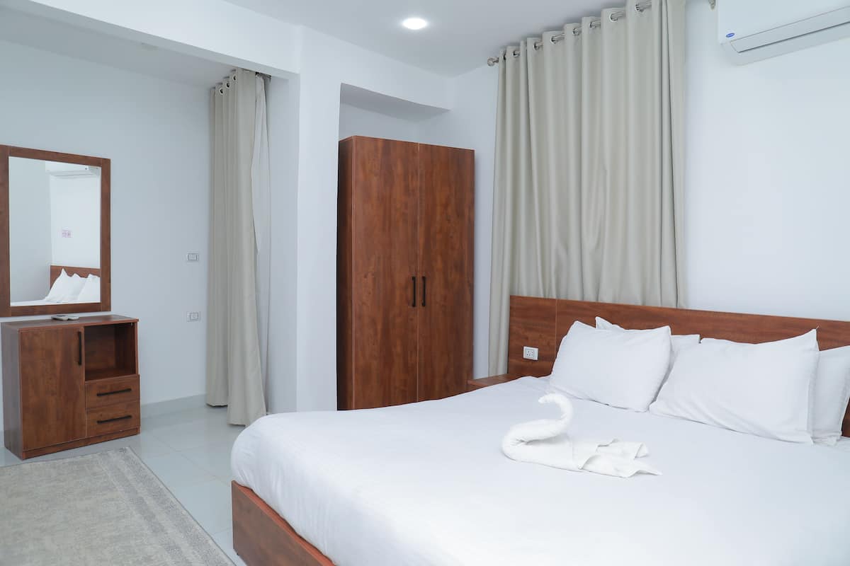 A bedroom with a bed, a wooden wardrobe, a mirror, and a window with curtains.