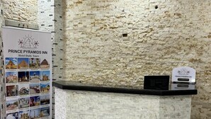 Zona de recepción con pared de textura de piedra, un mostrador de recepción y un tablón de anuncios que muestra las comodidades del hotel y atracciones turísticas.