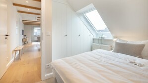 Quarto com claraboia, cama com travesseiros e vista para a área de estar adjacente.