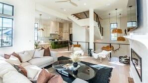 Un soggiorno moderno con un divano, un tavolino e un camino. Sullo sfondo, un'area cucina con un tavolo da pranzo e una scala che conduce a un piano superiore.