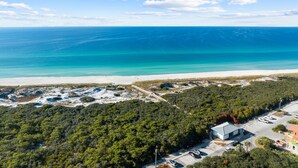 Vista aerea di una zona costiera con spiaggia, fitta foresta e un edificio con parcheggio.