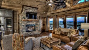 A cozy living room with a stone fireplace, leather furniture, and large windows offering a view of the mountains.