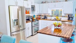 Une cuisine moderne avec des armoires blanches, des appareils en acier inoxydable, un îlot central en bois agrémenté de fruits et un revêtement mural coloré.