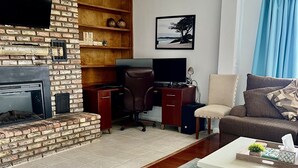 Un salon avec une cheminée, un bureau, un ordinateur, un canapé et un téléviseur fixé au mur en briques.
