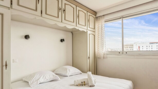 A neatly made bed with white linens, a set of towels, and a mirror above it. - Appartement Leroy, balcon - Welkeys (Clichy)