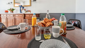 A breakfast table set with croissants, juice, and coffee, with a mirror and decorative items on the wall. - Appartement Leroy, balcon - Welkeys (Clichy)