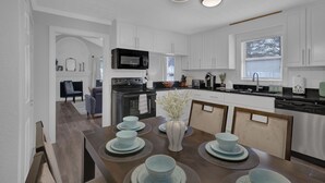 A modern kitchen with white cabinets, a black microwave, and a dining area with a table set for four. - Stylish Duplex! New Remodel! Minutes from Atlanta! (Norcross)