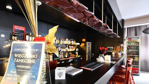 A bar area with a menu board, bar stools, and a variety of bottles on shelves. - Geovita Dzwirzyno (Kołobrzeg)