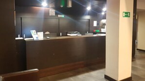 Un comptoir d’accueil en bois foncé, une horloge et un panneau vert indiquant la sortie de secours.