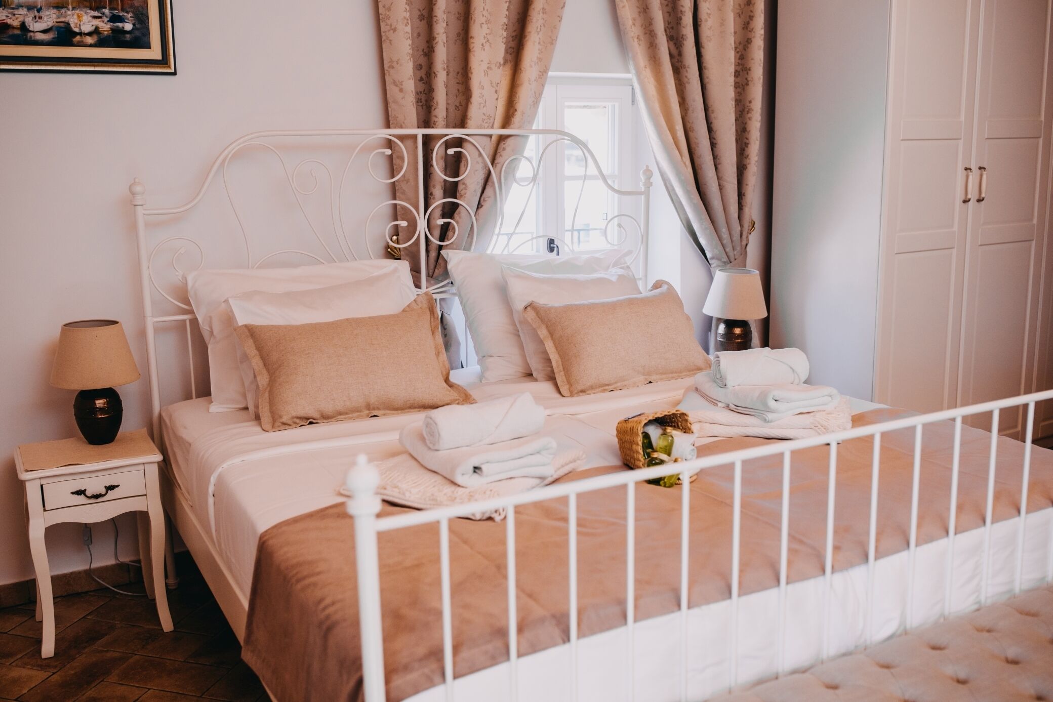 A neatly made bed with a white metal frame, beige bedding, and a small bedside table with a lamp.