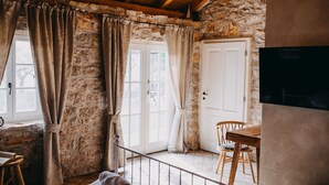 A rustic room with stone walls, a wooden ceiling, a dining table with chairs, and a television.