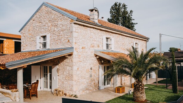 A stone house with a pool, outdoor furniture, and a palm tree.