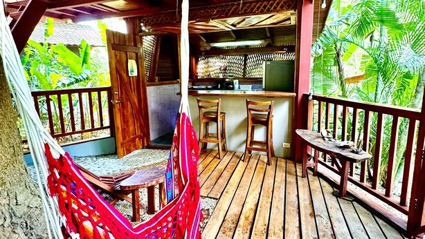 Eine Holzterrasse mit einer Hängematte, einem kleinen Tisch und Stühlen.