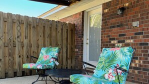 A patio with two chairs and a table, a wooden fence, and a brick wall.
