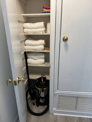 Ein Schrank mit Regalen, voll mit gefalteten Handtüchern und einem Staubsauger.