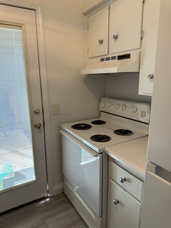 Eine kleine Küche mit einem weißen Herd, Schränken und einer Tür mit Frostglasfenster.