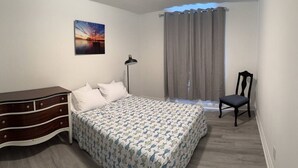 A bedroom with a bed, a dresser, a chair, a lamp, and a painting on the wall.