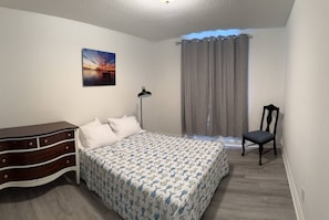 Ein Schlafzimmer mit einem Bett, einem Schminktisch, einem Stuhl, einer Lampe und einem Bild an der Wand.
