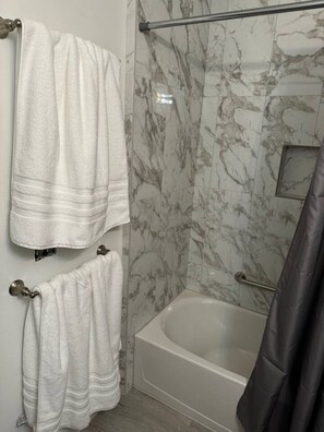 Ein Badezimmer mit Badewanne, zwei Handtüchern, einer Duschvorhang und Marmorwänden.
