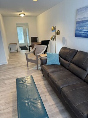 Ein Wohnzimmer mit einem braunen Ledersofa, einer blauen Bank, einer Stehlampe und einem Gemälde an der Wand.