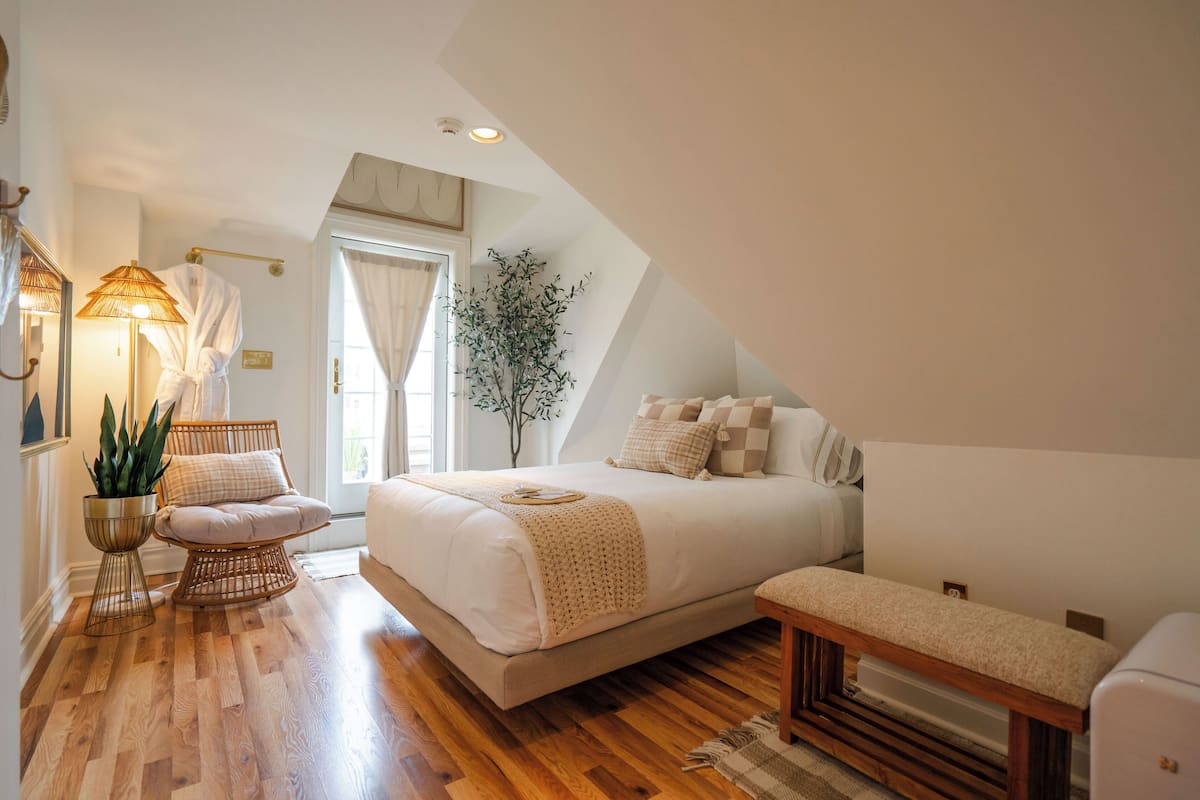 A bedroom with a large bed, a bedside table, a chair, a floor lamp, and a potted plant.