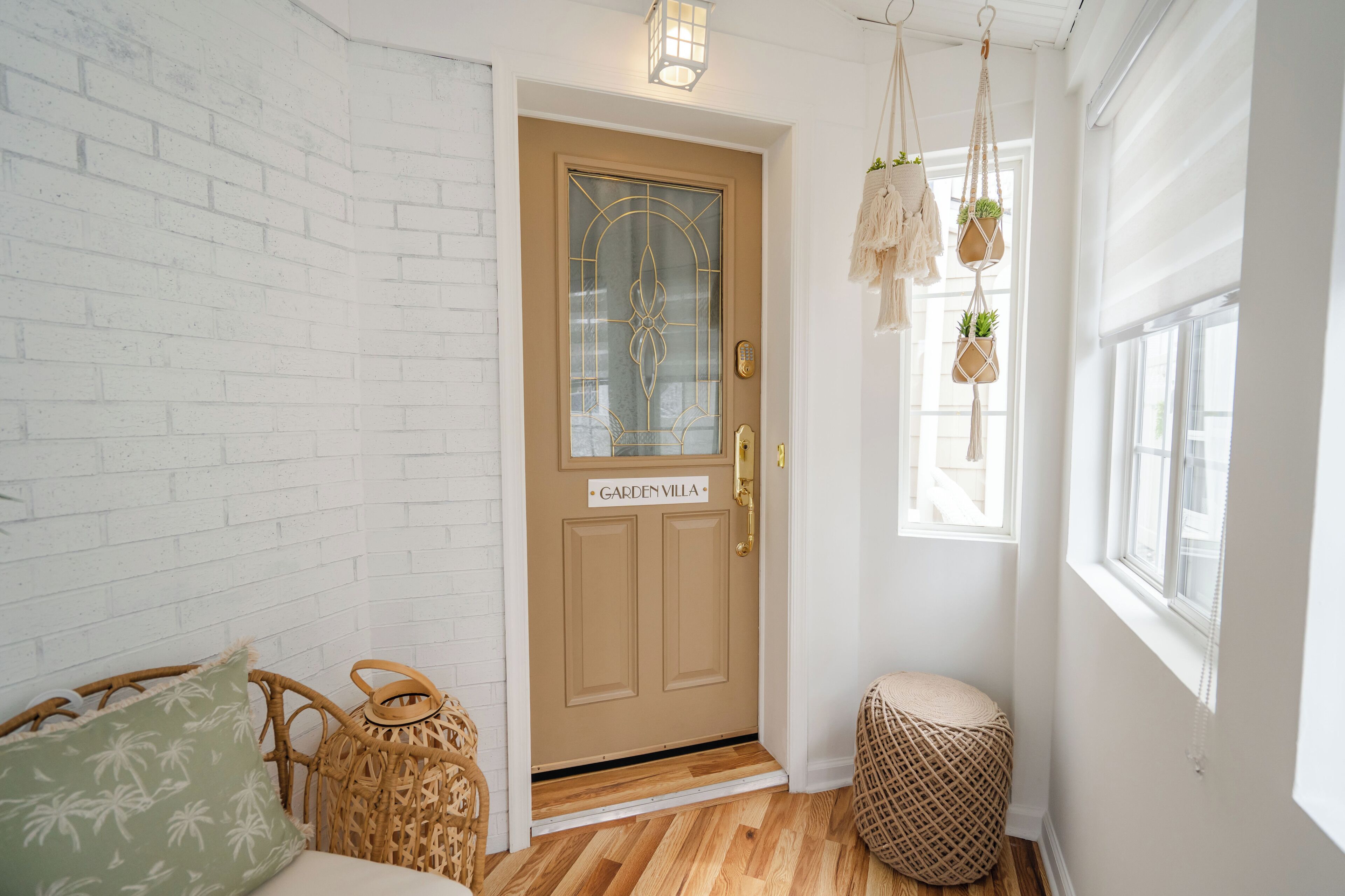 A cozy entryway with a beige door labeled "GARDEN VILLA," wicker furniture, and a small round ottoman.