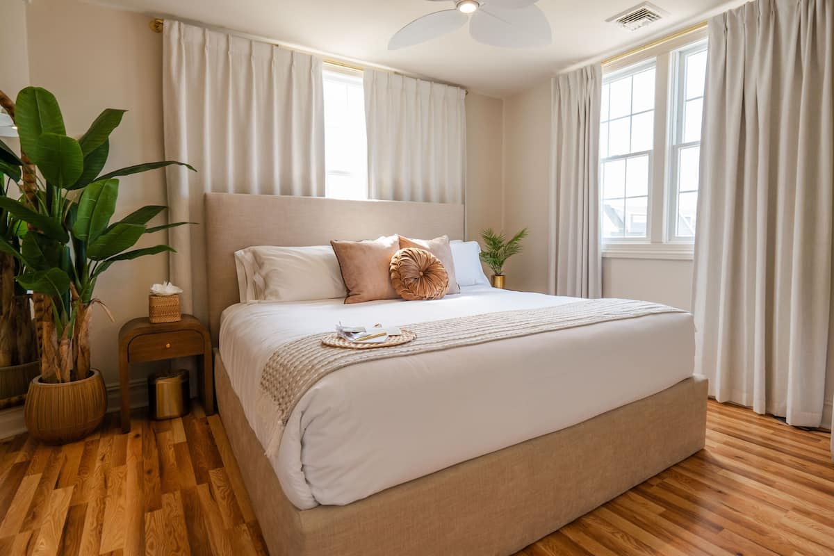 A bedroom with a large bed, wooden flooring, and a ceiling fan.