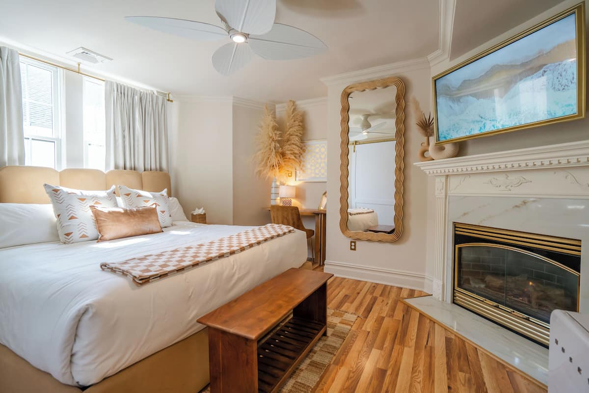 A bedroom with a large bed, a bench, a fireplace, and a ceiling fan.