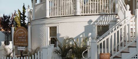 A two-story building with a curved facade, a balcony with white railings, and a staircase leading to the entrance.
