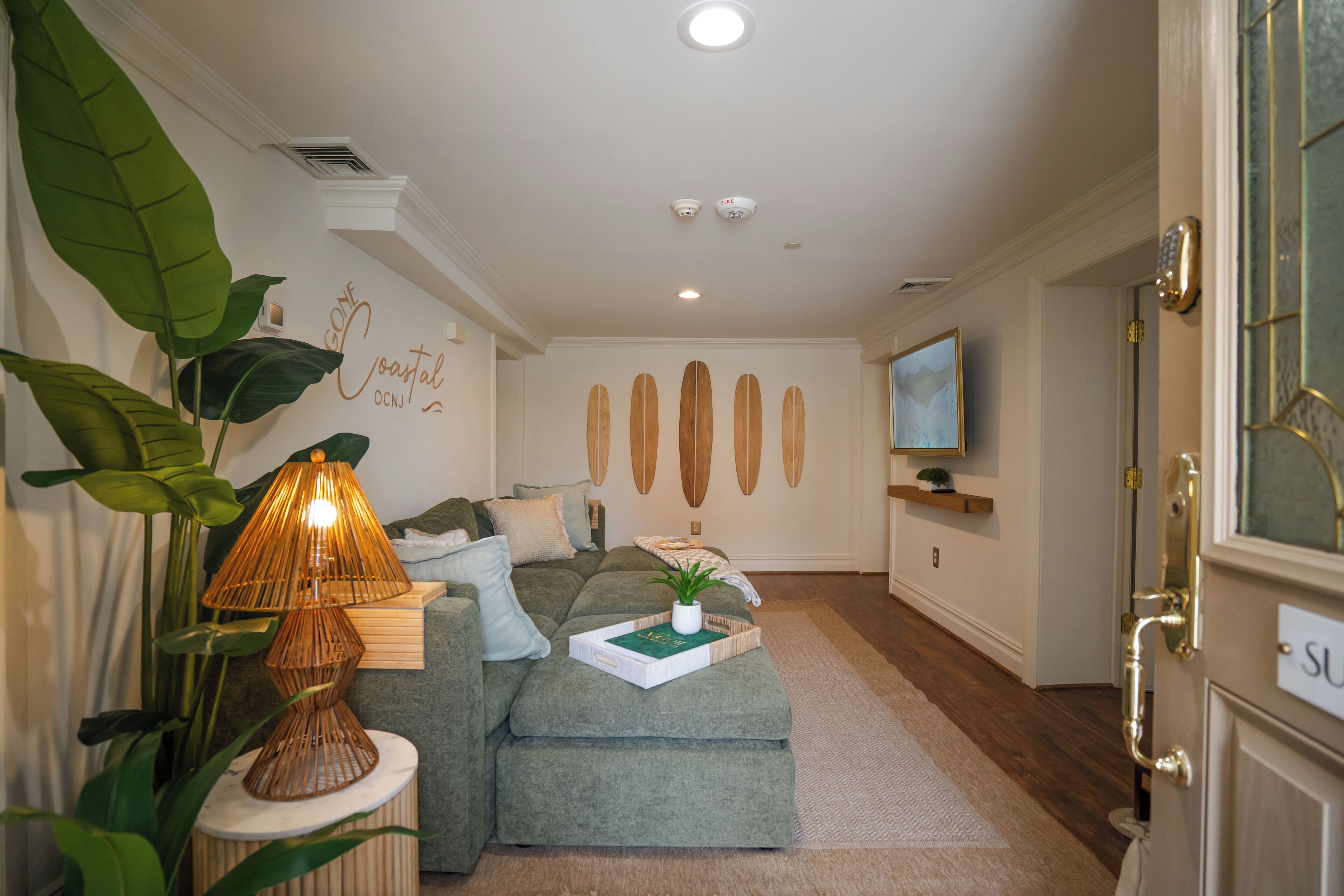 A living room with a sofa, a lamp, a plant, and a wall with surfboards.