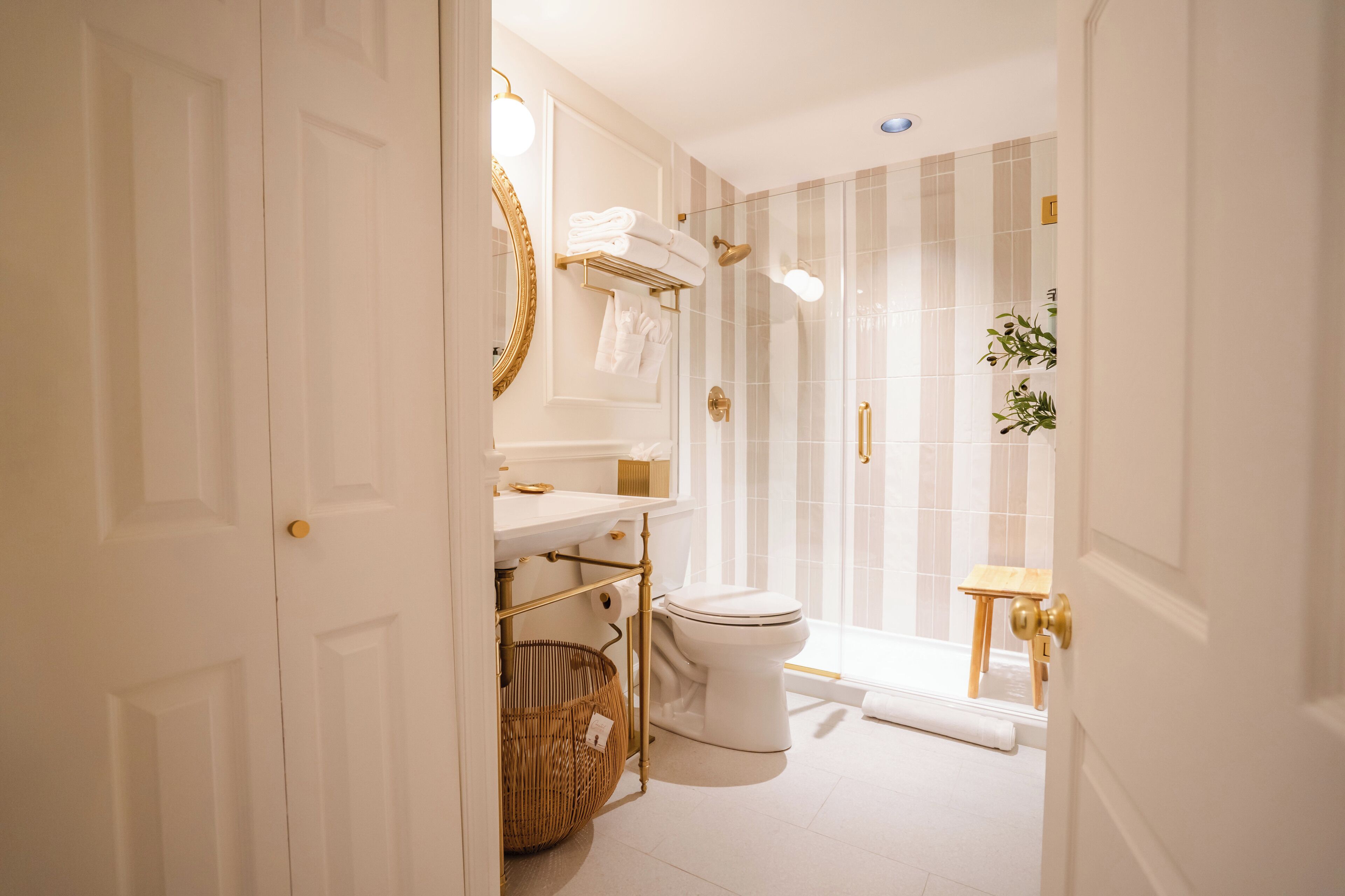 Ein Badezimmer mit Toilette in Weiß, einem Waschbecken mit Goldarmatur und einer Dusche mit Glastür.