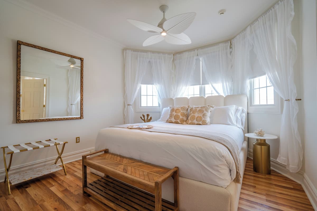 A bedroom with a large bed, a ceiling fan, a bedside table, and a bench.