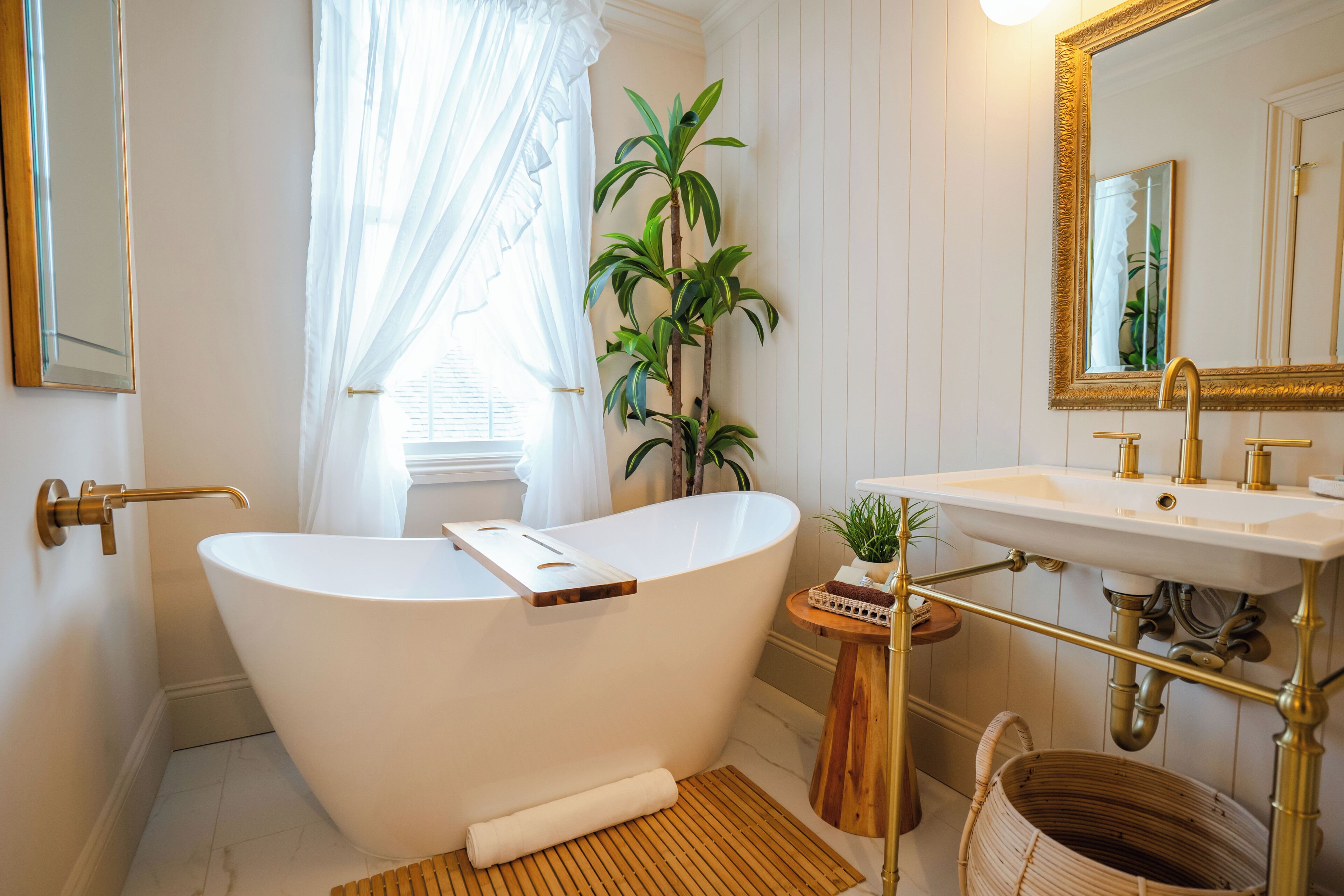 A bathroom with a freestanding bathtub, a sink with a gold faucet, a mirror with a gold frame, and a potted plant.