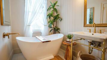 A bathroom with a freestanding bathtub, a sink with a gold faucet, a mirror with a gold frame, and a potted plant.