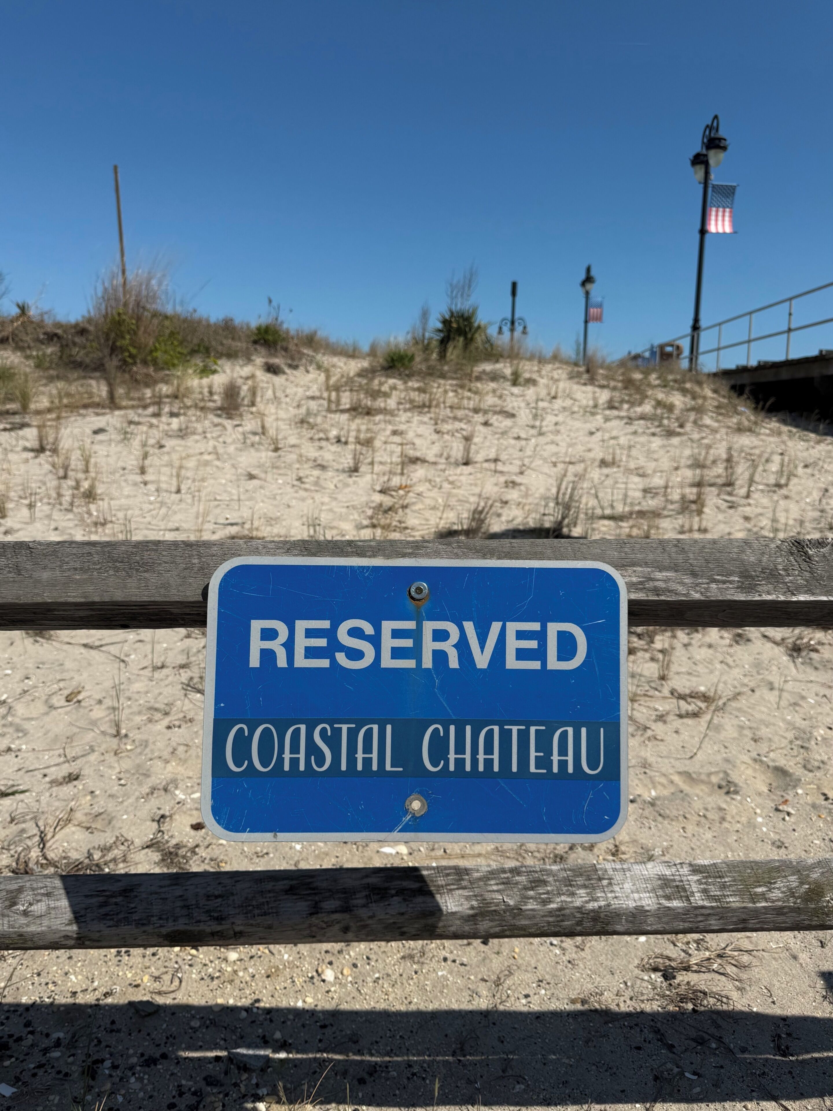 A blue sign with white text stating 'RESERVED COASTAL CHATEAU' on a wooden fence.