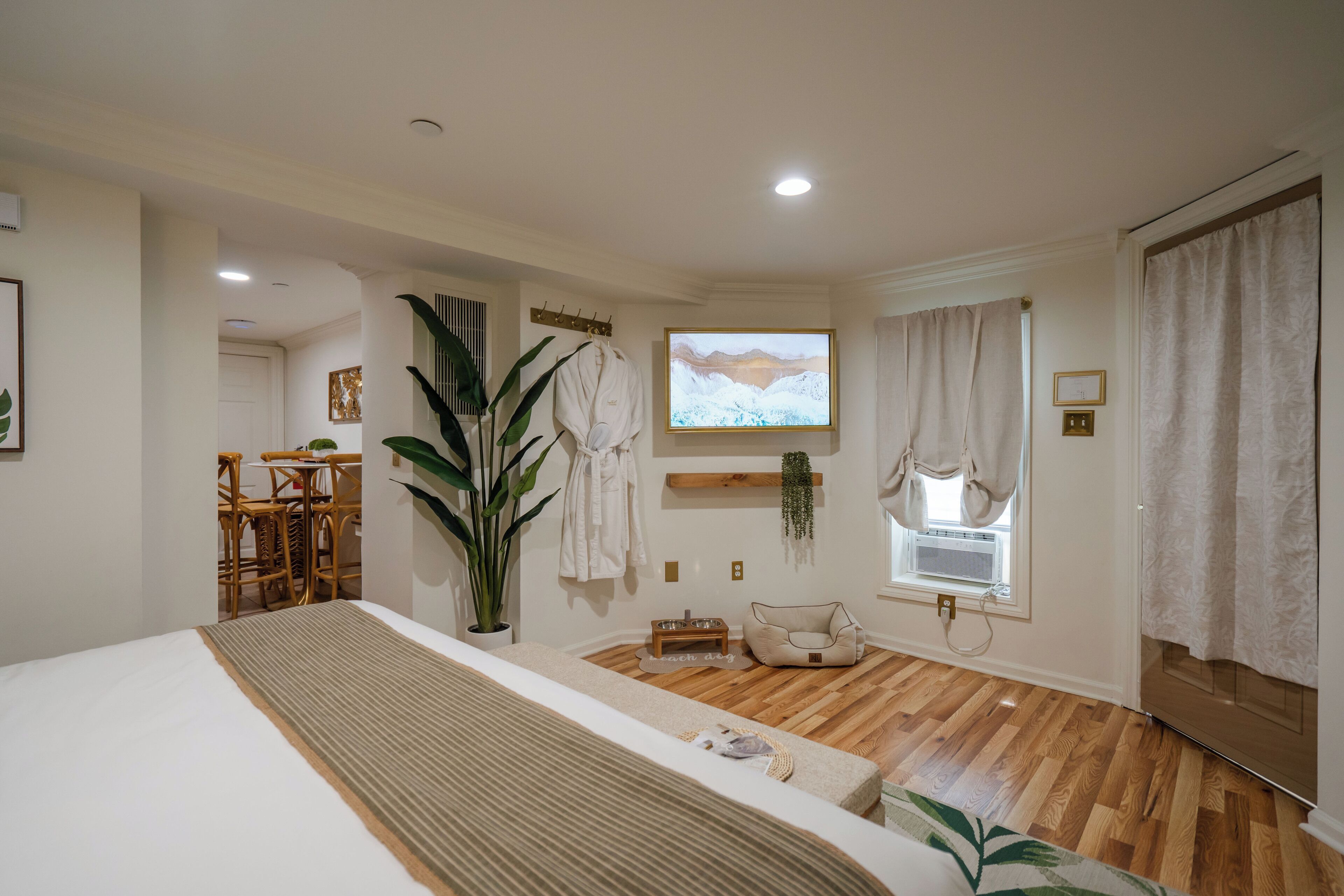 Una habitación de hotel moderna con una cama grande, suelo de madera, televisión, planta y un rincón de descanso acogedor.