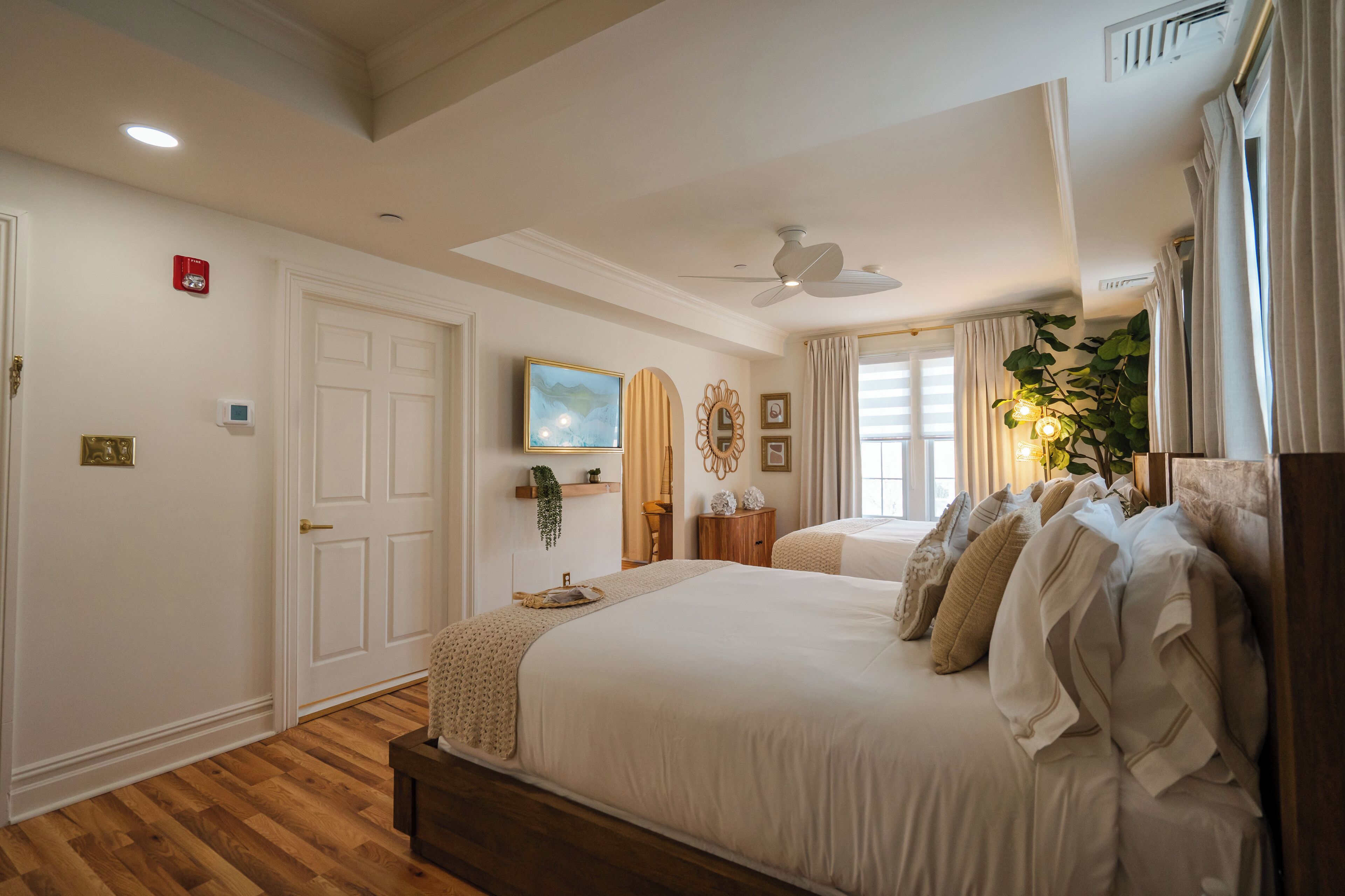 Quarto com cama grande, ventilador de teto, televisão montada e janela com cortinas.