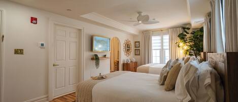 A bedroom with a large bed, a ceiling fan, a mounted TV, and a window with curtains.
