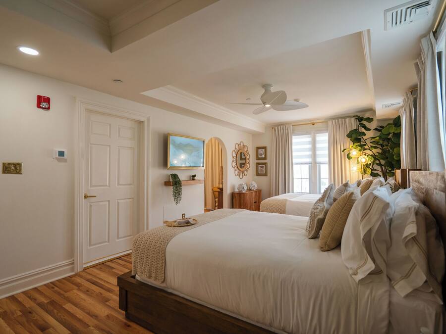 Quarto com cama grande, ventilador de teto, televisão montada e janela com cortinas.
