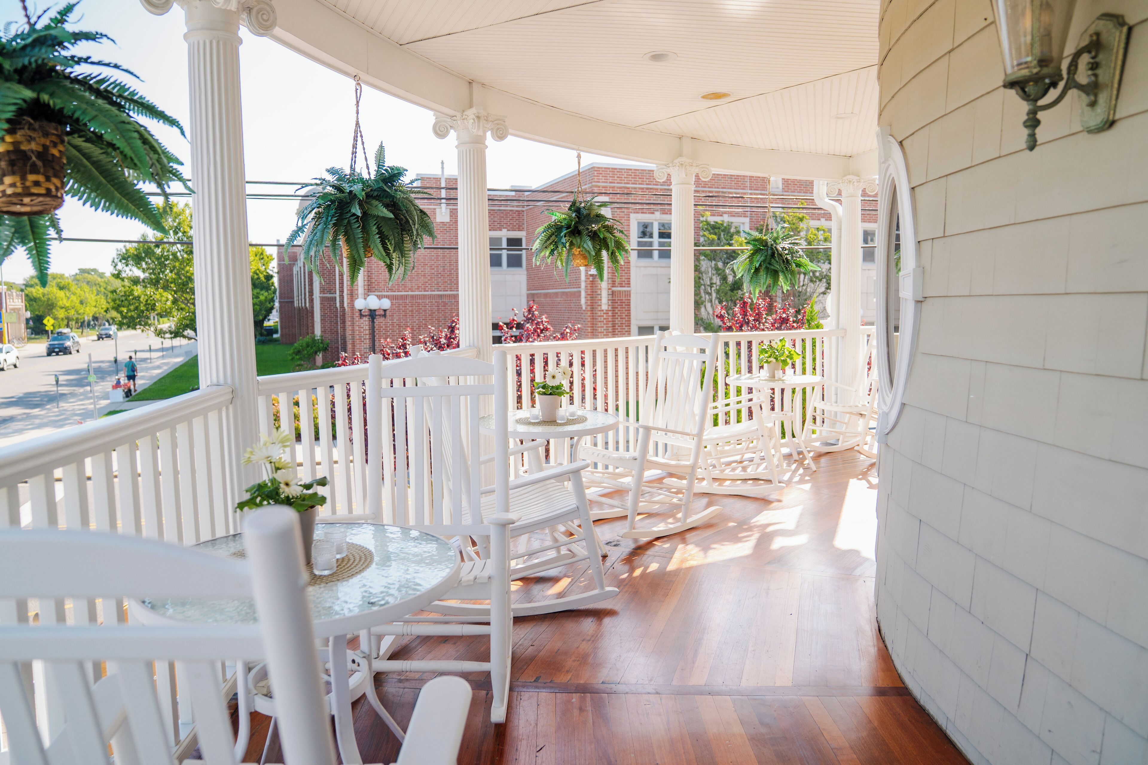 A covered porch with white railings, wooden flooring, and potted plants.